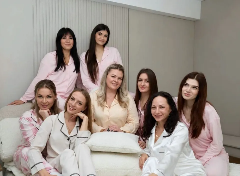 Echipa K.O: opt meștere în pijamale roz și albe, zâmbind, în salon